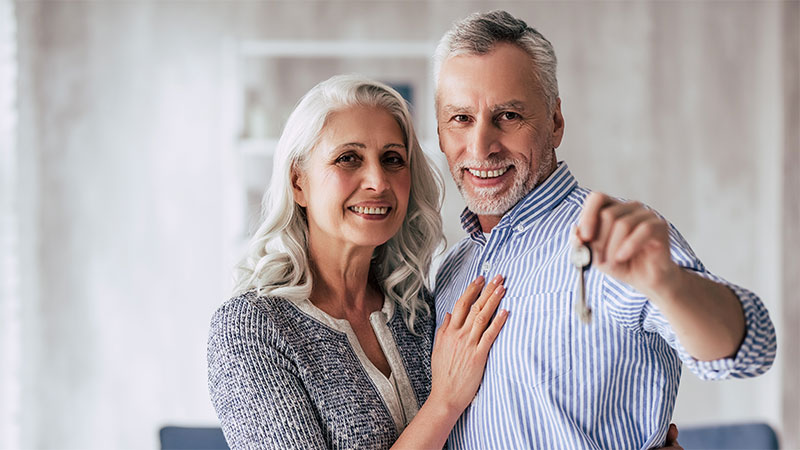 older couple with man holding out keys to new home with big smiles